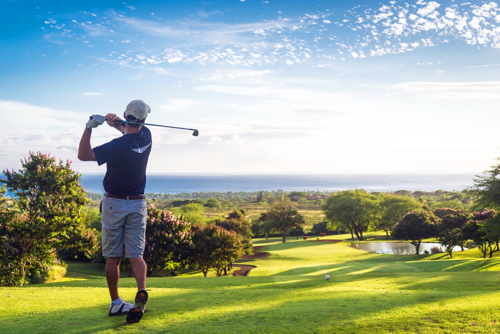 Golfer hitting ball down hill towards scenic view